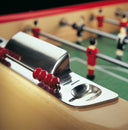 Close-up of a foosball table with a red player figure and metal rod.